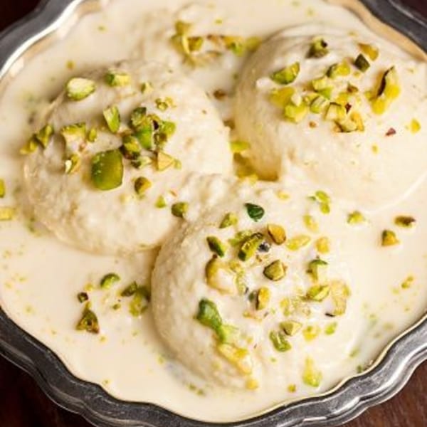 Three Indian rasmalai desserts in a silver dish, garnished with chopped pistachios.
