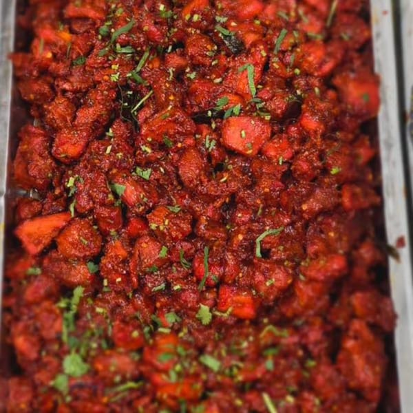 Close-up of vibrant red Indian chicken curry, garnished with fresh green herbs in a metal serving tray.