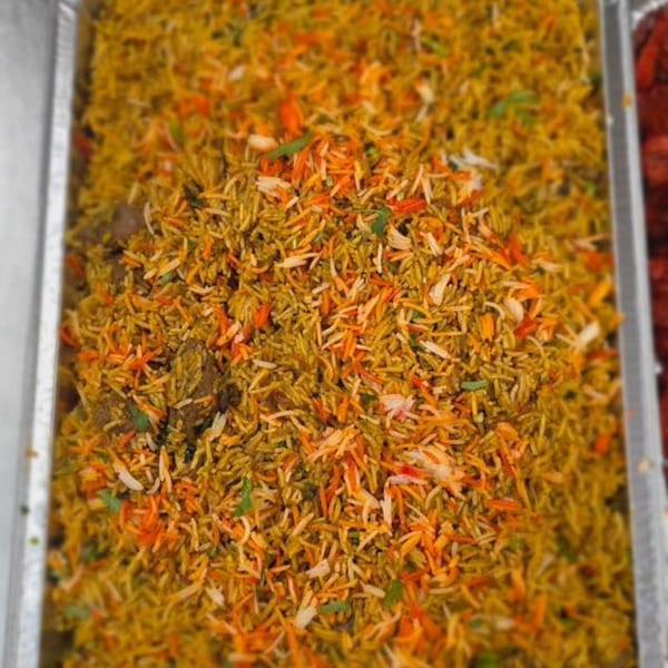 Close-up of vibrant Indian biryani with yellow, orange, and white rice grains in a foil tray.