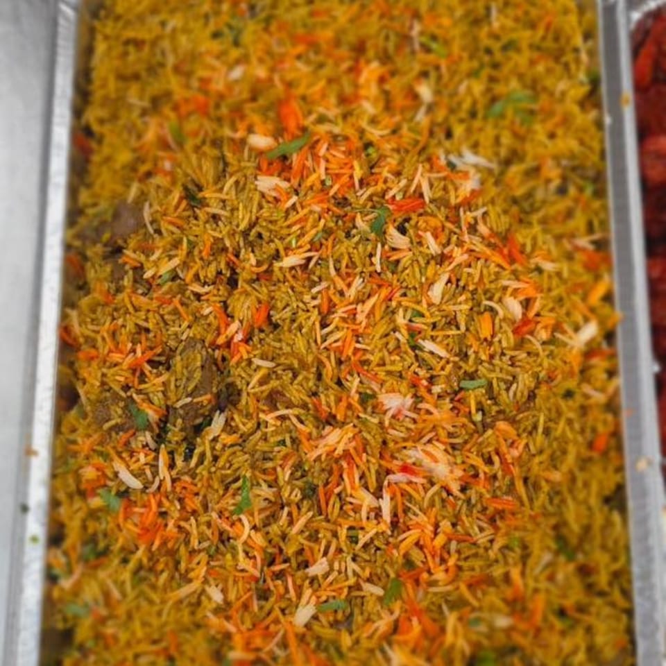 Close-up of vibrant Indian biryani with yellow, orange, and white rice grains in a foil tray.