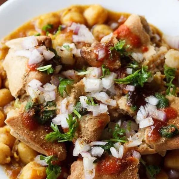 Close-up of Indian chaat with crispy bread, chickpeas, onions, cilantro, and sauces.