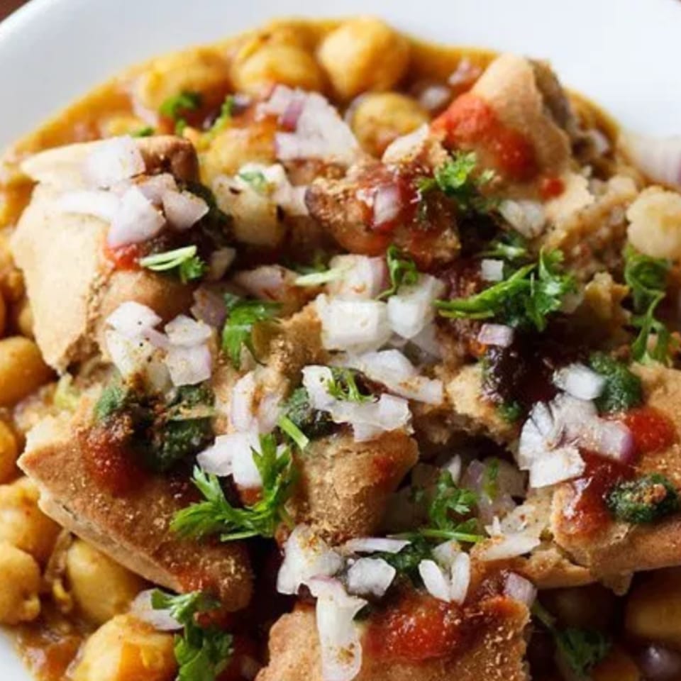 Close-up of Indian chaat with crispy bread, chickpeas, onions, cilantro, and sauces.