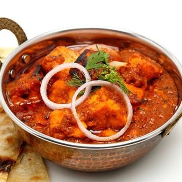 Indian chicken curry in a copper bowl, garnished with onion rings and fresh herbs.