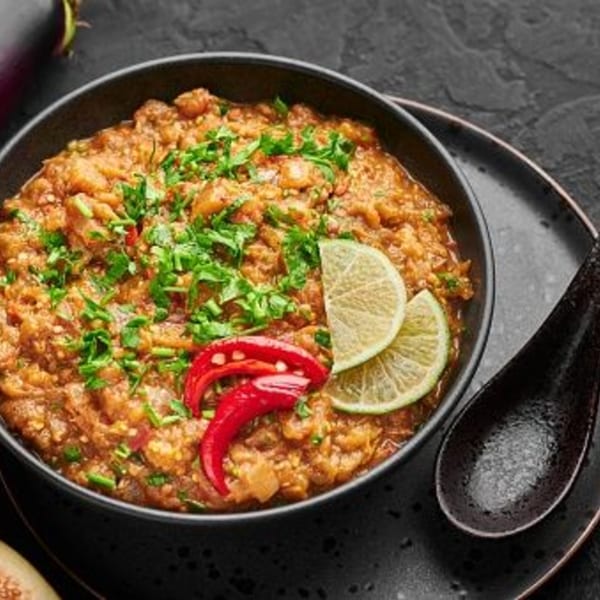 Indian baingan bharta, an eggplant dish, garnished with cilantro, lime, and red chilies.