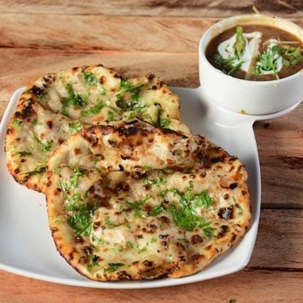 Two pieces of garlic naan bread with a side of dal makhani on a white plate.