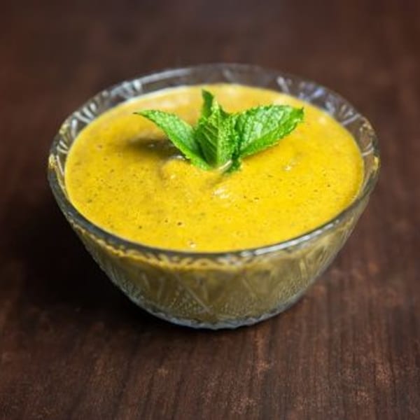 A glass bowl of vibrant yellow Indian curry sauce, garnished with fresh mint leaves, on a wooden surface.