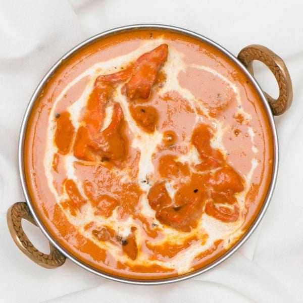 Overhead view of Indian butter chicken, a rich orange curry with cream swirls, in a metal karahi.