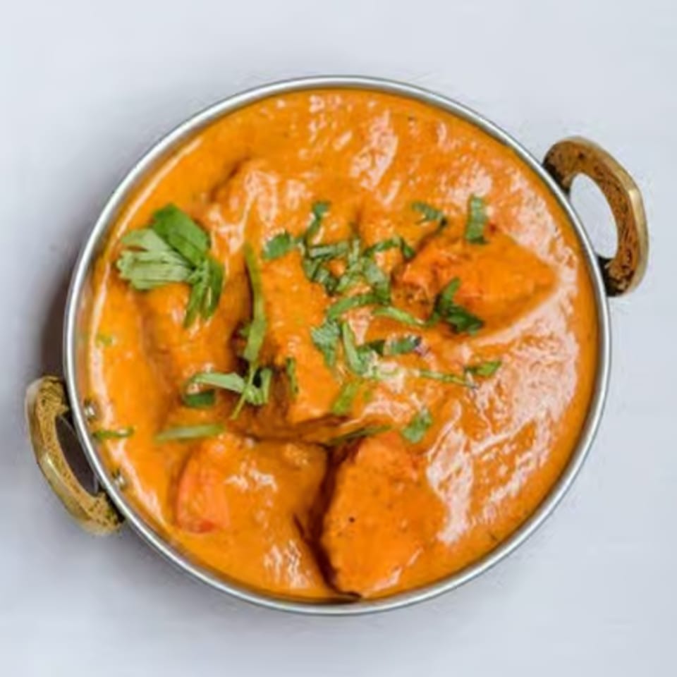 Curry House's vibrant orange chicken tikka masala, garnished with fresh cilantro in a metal bowl.